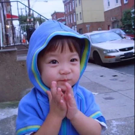 Aaron as a toddler in a blue hooded jacket on a city sidewalk