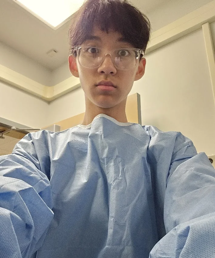 Aaron in a blue isolation gown and clear glasses during the UPenn Summer Mentorship Program