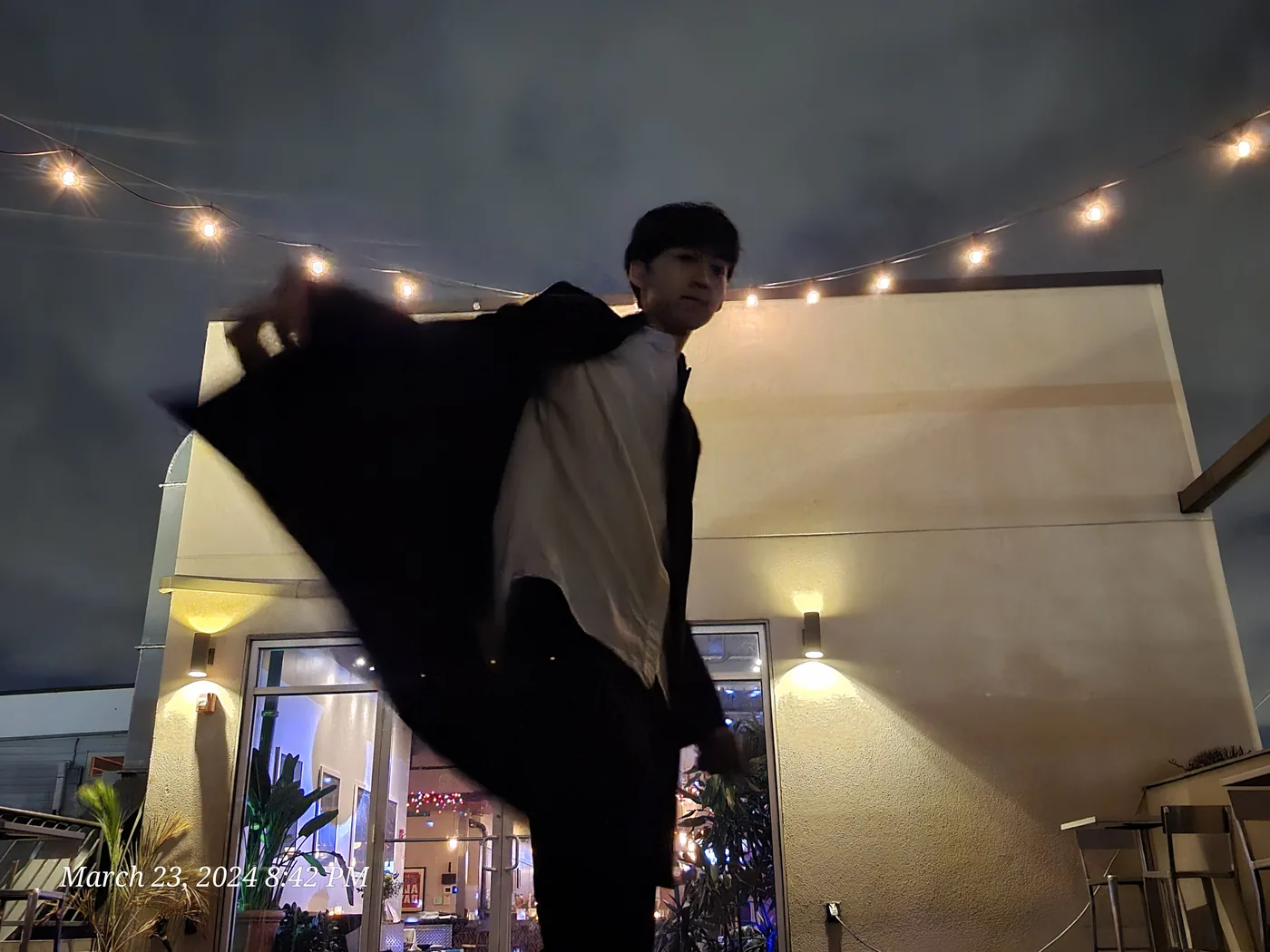 Aaron in a long coat under string lights