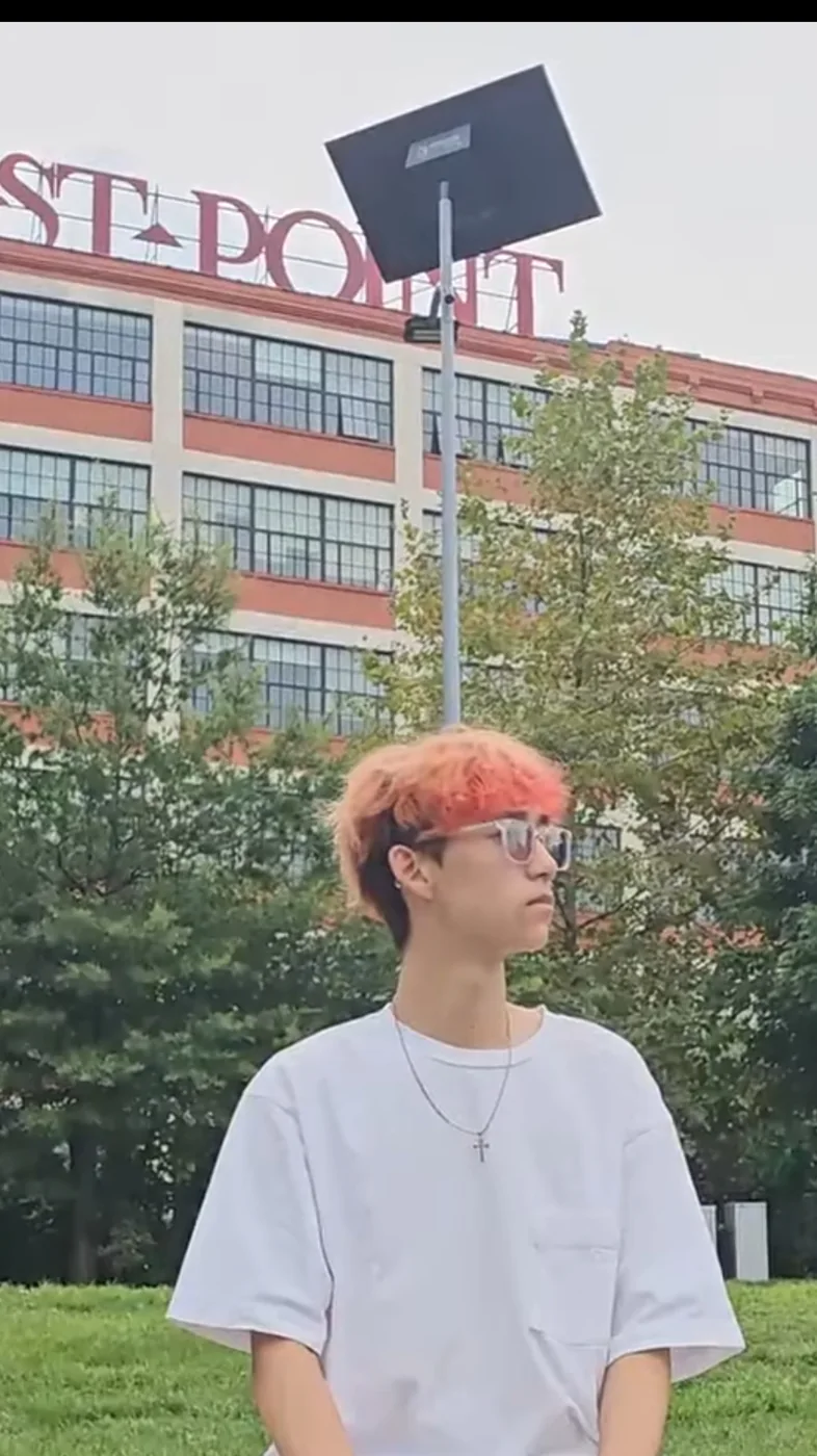 Aaron with orange-dyed hair sitting outdoors in front of a brick building