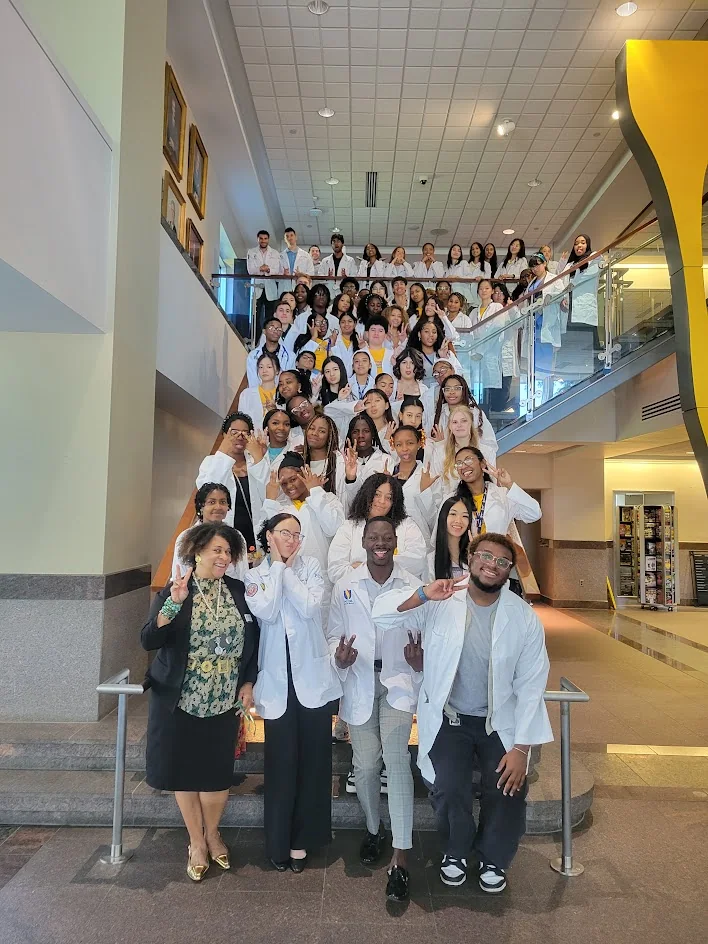 A large group of students in white coats posing on a staircase