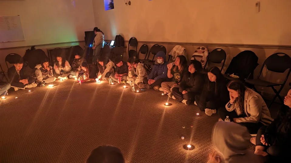 A youth group sitting in a circle around candles in a dim room