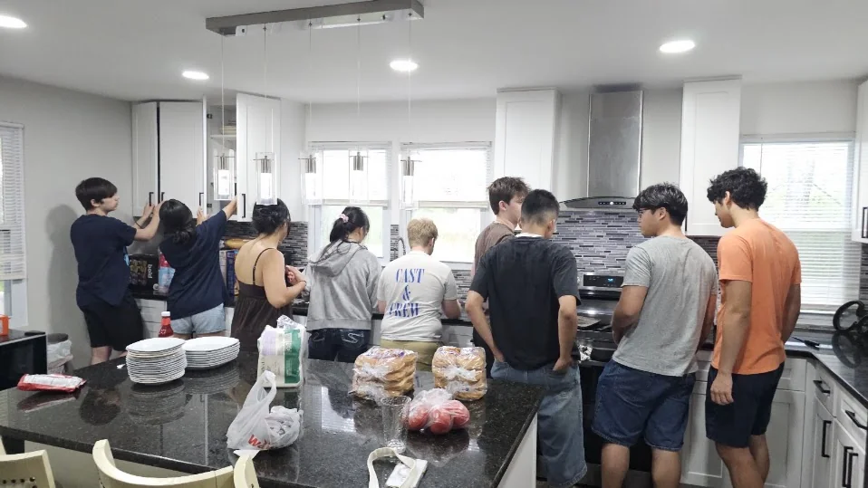 A group of teens and adults preparing food together in a kitchen
