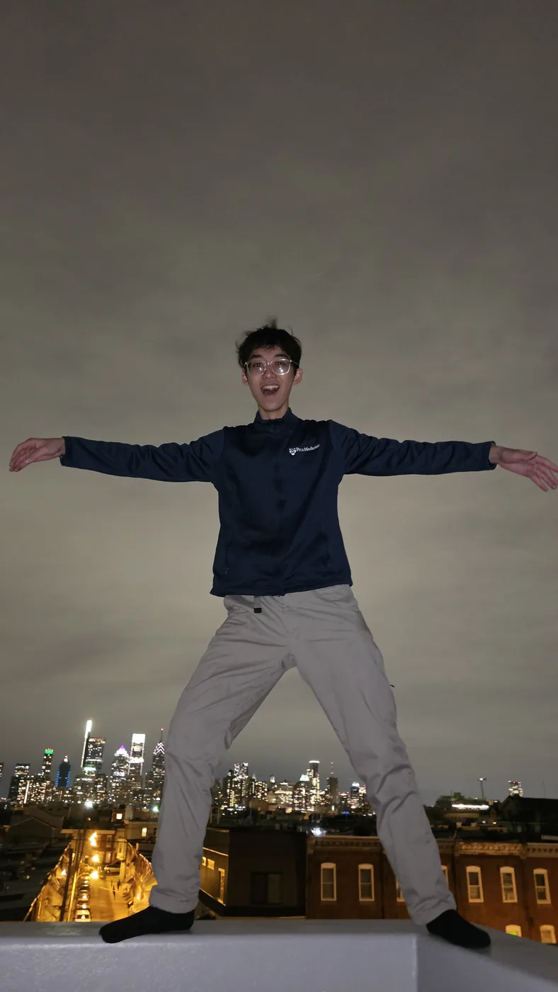 Aaron with arms spread on a rooftop above the city at night