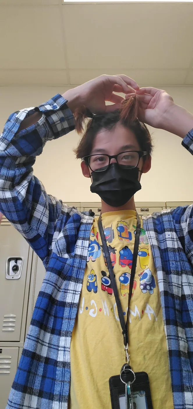 Aaron in a plaid shirt and school lanyard by the lockers