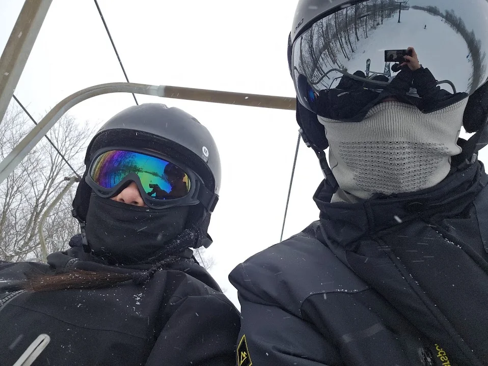 Two skiers in helmets and goggles on a chairlift