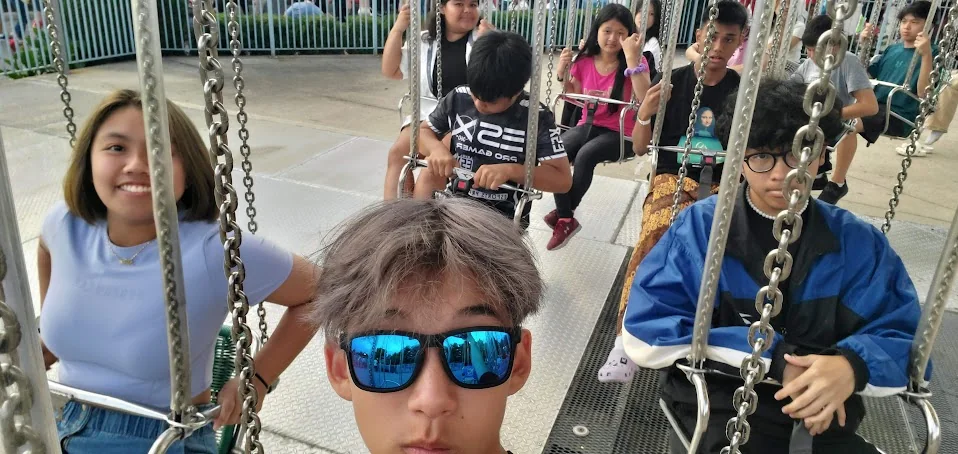 Aaron in sunglasses taking a selfie on a swing ride with friends