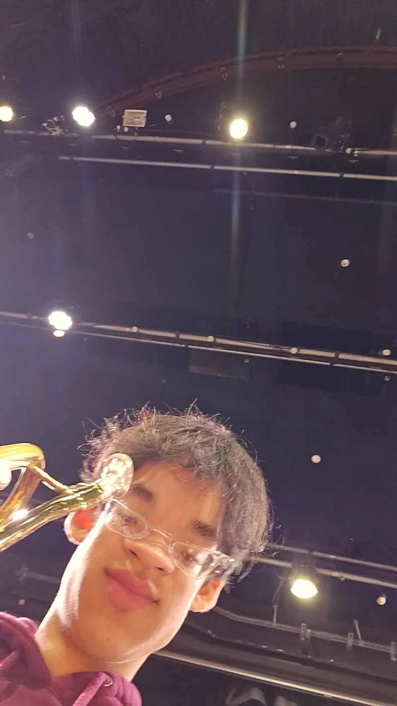 Aaron holding a trumpet on a stage under bright lights