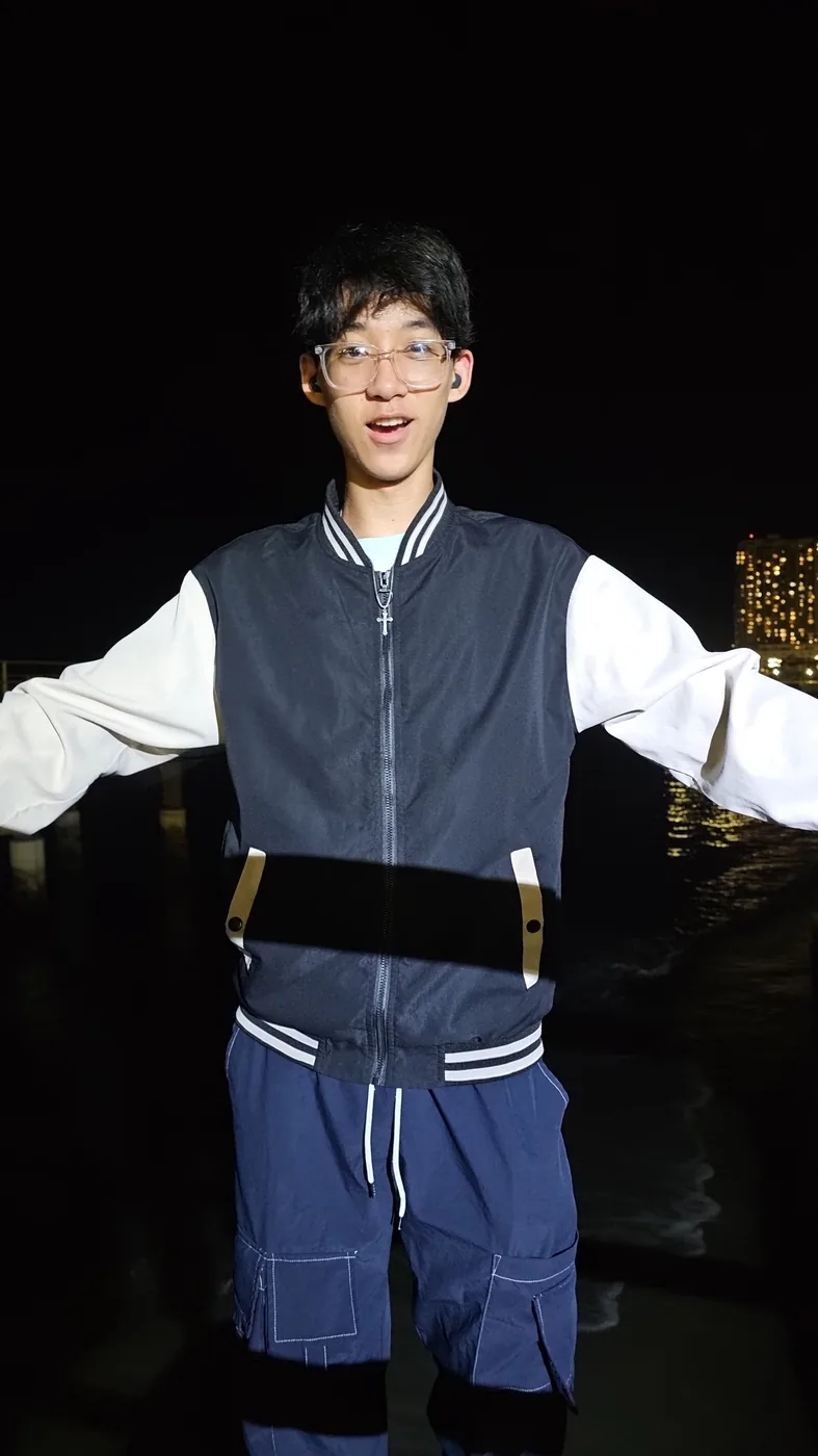 Aaron in a varsity jacket on a waterfront at night